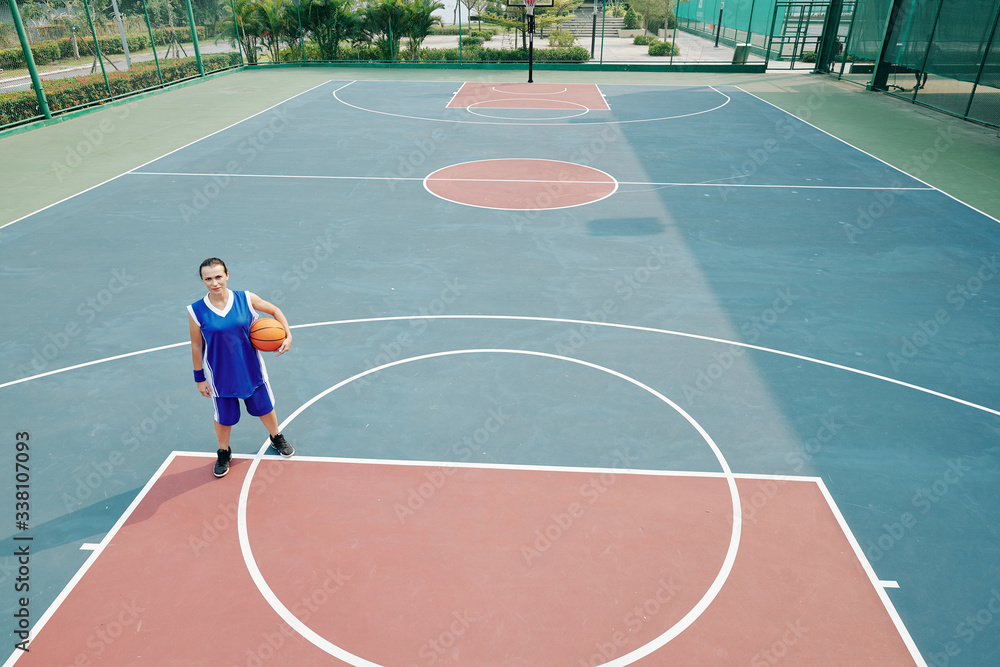 Fototapeta premium Young woman playing alone on outdoor basketball court