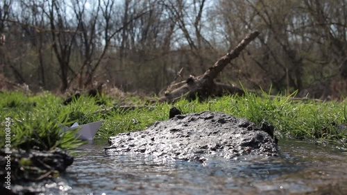 Paper ship. A paper boat is floating on the water. White paper ship. A boat  floats on water. A paper boat is floating on the river. Forest river. River runs along a forest.