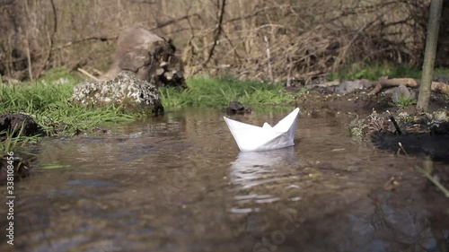 Paper ship. A paper boat is floating on the water. White paper ship. A boat  floats on water. A paper boat is floating on the river. Forest river. River runs along a forest.
