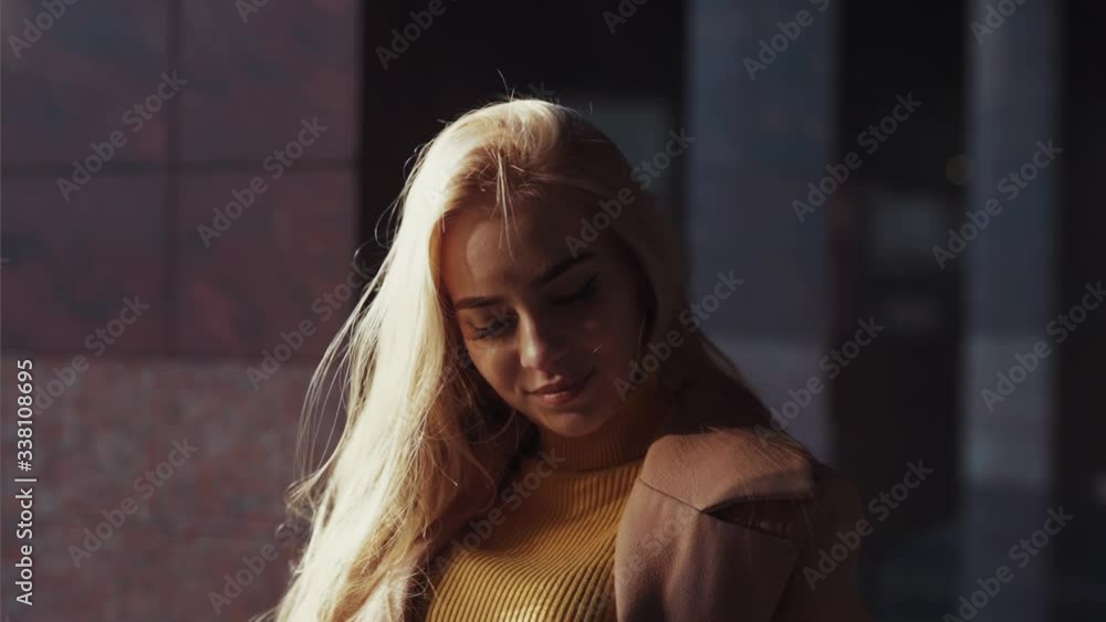 Appealing young sexy blonde woman wearing coat looking at camera confident with lovely hair blowing in wind standing in beautiful modern business city district. Appealing young sexy blonde woman wearing coat looking at camera confident with lovely hair blowing in wind standing in beautiful modern business city district.