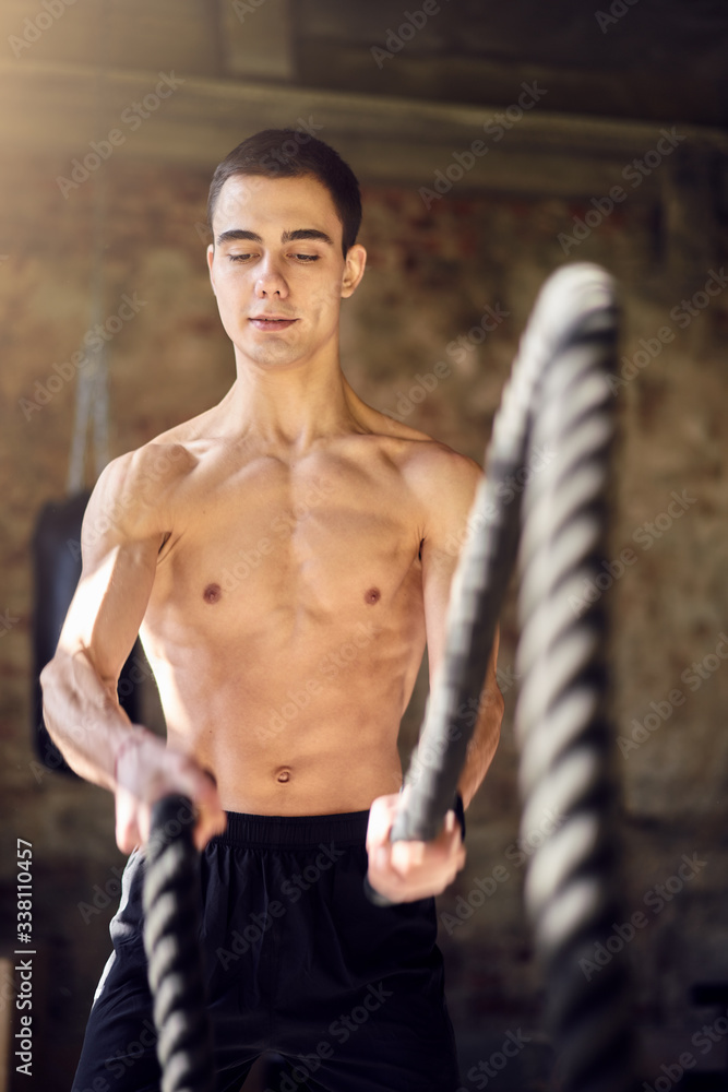 Fototapeta premium Sportsman in training with ropes against background of brick wall