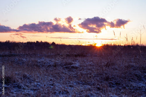 the last rays of the setting sun. field with yellow grass sprinkled with snow