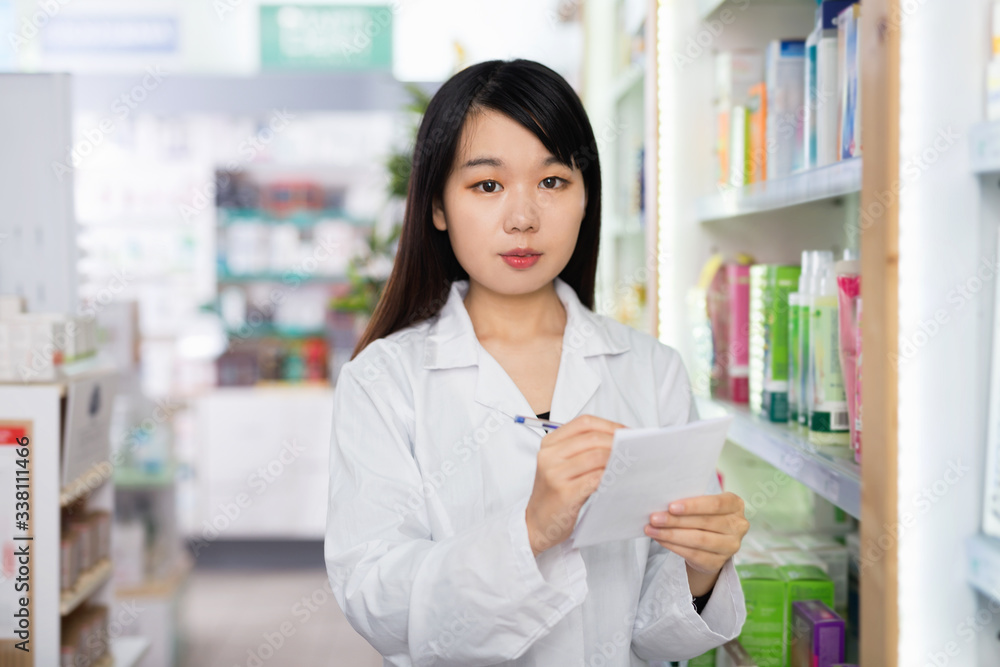 Chinese woman pharmacist keeps track of drugs in interior of pharmacy