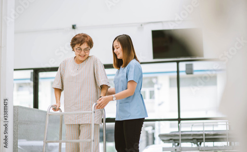 young physical therapist helping senior patient in using walker during rehabilitation