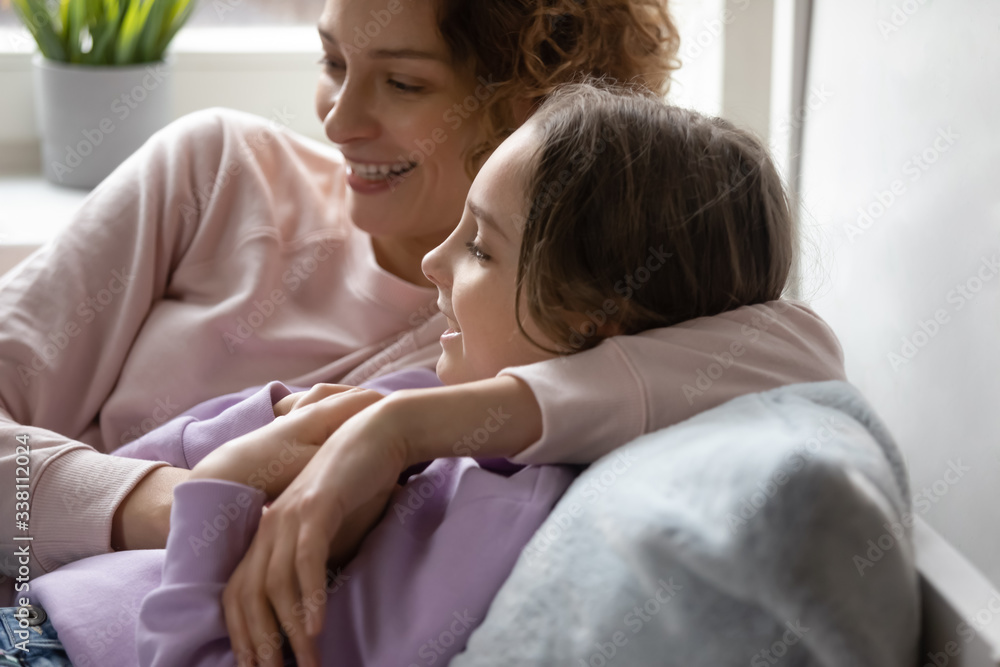 Obraz premium Smiling mom embracing teen daughter resting together at cozy home. Happy family young adult parent mother and cute teenage school girl bonding, talking, enjoying sweet moment relaxing lying in bed.