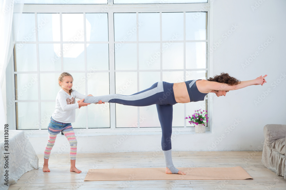 Fitness adult woman with her child. Morning exercises, yoga - do at home all together. Grandmother and granddaughter doing yoga exercise home. Mother and daughter do gymnastics exercises.