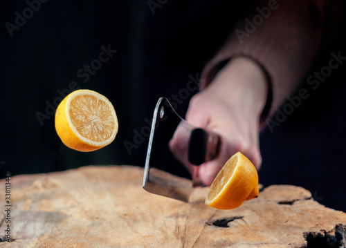 Hand with knife slicing a lemon in half on the wooden board