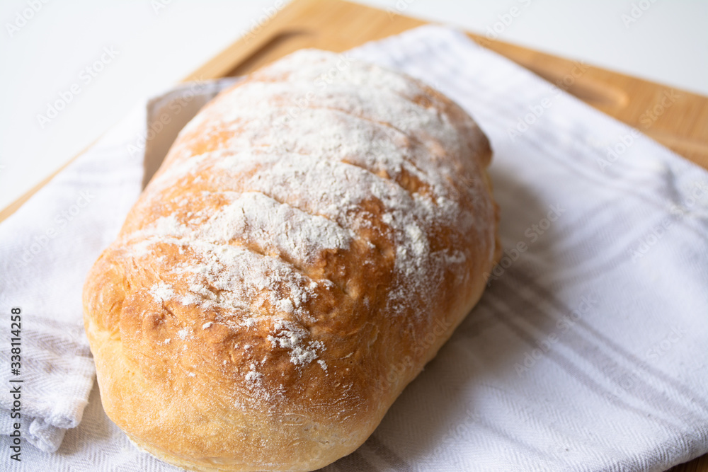 A loaf of homemade fresh bread with flour sprinkled on top in a kitchen towel on wooden cutting board with slices A loaf of homemade fresh bread with flour sprinkled on top in a kitchen towel on wooden cutting board with slices