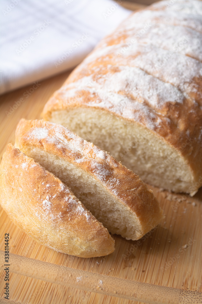 A loaf of homemade fresh bread with flour sprinkled on top in a kitchen towel on wooden cutting board with slices A loaf of homemade fresh bread with flour sprinkled on top in a kitchen towel on wooden cutting board with slices
