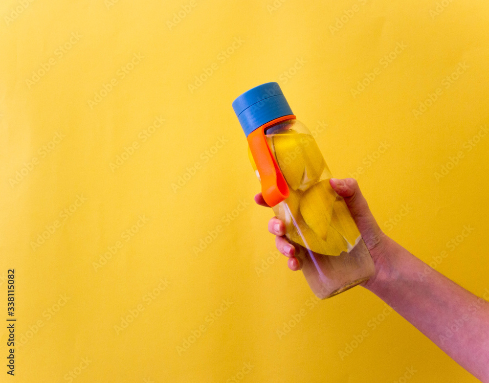 Flat lay style concept of healthy lifestyle, sport and fitness at home.  Hand holding bottle of water with lemons on yellow background. Top view.