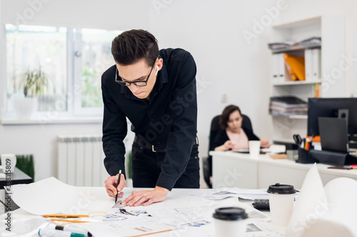 Young attractive male fashion designer leaning on the office desk, working on a sketch