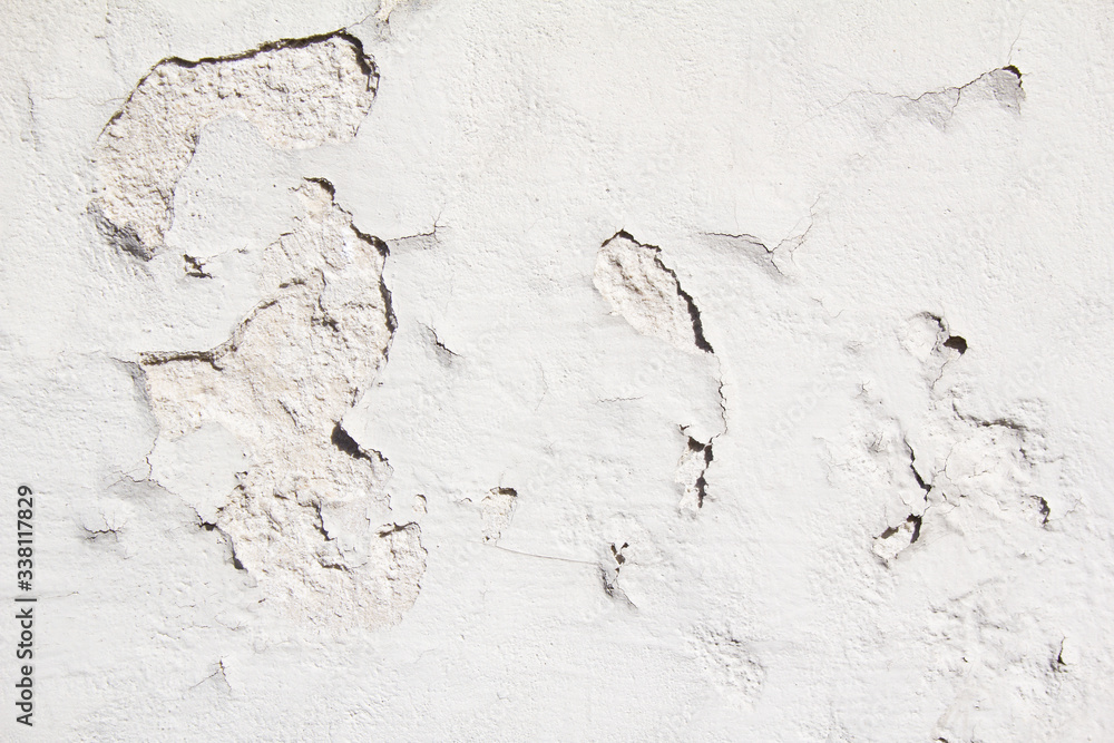 Old weathered white wall with rough surface and peeling paint and plaster texture background.