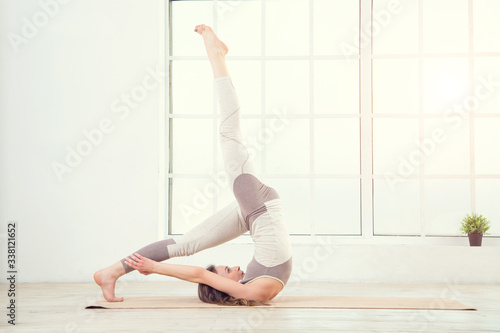 Pilates woman. Woman doing yoga exercises on mat in gym. Woman in the window background. Space for text. Woman exercising fitness in gym near the window.