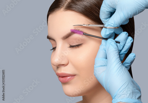 Makeup artist comb and trim the eyebrows with scissorss to a woman before staining with henna. Women's cosmetology in the beauty salon.