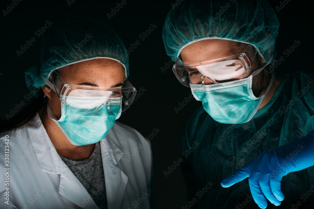 Portrait of Close up of two woman and man doctors working wearing medical surgical mask, glasses, medical cap and virus protective clothing on black background with copy space. Portrait of Close up of two woman and man doctors working wearing medical surgical mask, glasses, medical cap and virus protective clothing on black background with copy space.