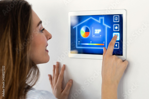 Photography Pretty young woman using the home automation system on digital tablet to regulate the temperature