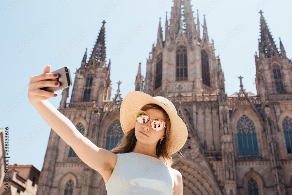 Fototapeta premium Young and happy tourist woman making selfie photo in front of cathedral in Barcelona