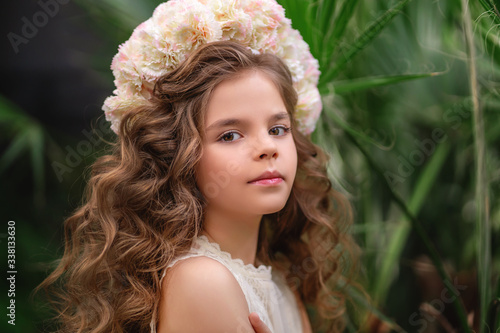 Cute smiling little girl with flower wreath on her head. Portrait of adorable small kid outdoors.