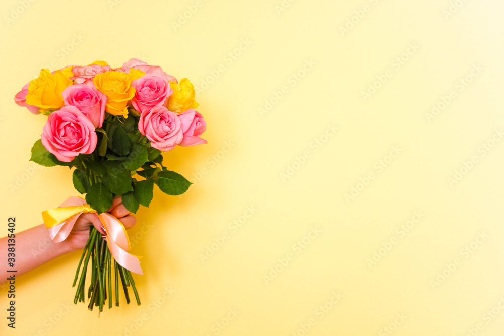 holding beautiful tender blossoming bouquet of yellow and pink roses on yellow background. Free copy space. Flowers delivery at home.