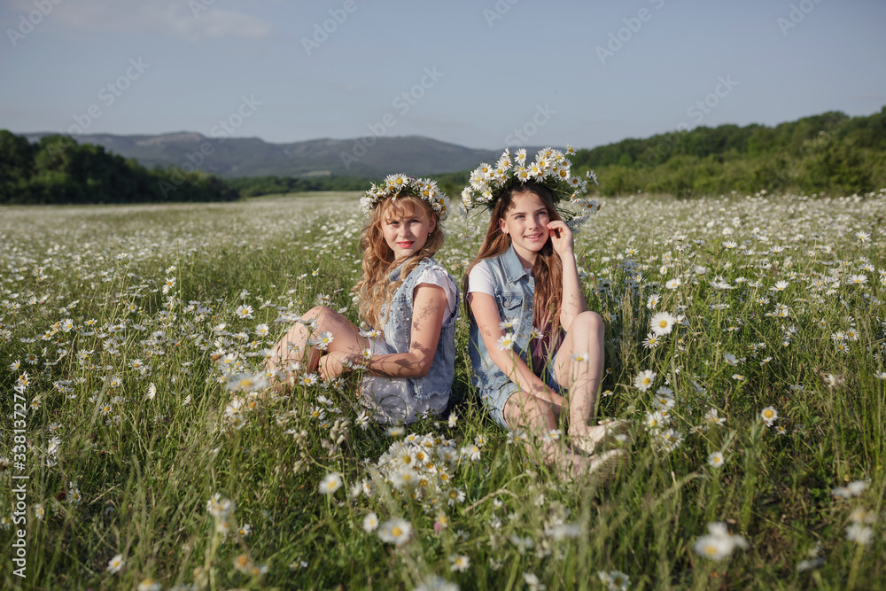 two cute teen girls in denim overalls walk in a daisy field two cute teen girls in denim overalls walk in a daisy field