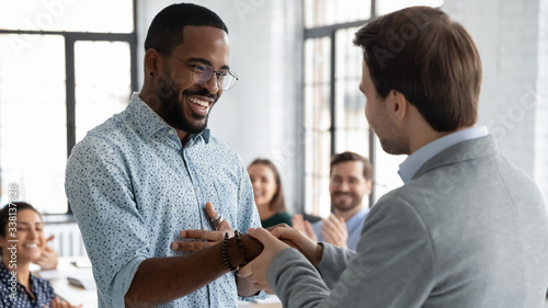 Caucasian businessman handshake African American male employee congratulate with work achievement or success, boss shake hand of biracial worker greeting with job promotion at office meeting photo