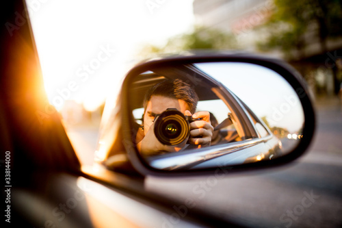 Photographer taking a self shot in the side mirrors of a car while the sun is shinning