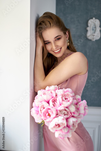 Valokuva Beautiful girl in a pink jumpsuit holding flowers in studio at the window