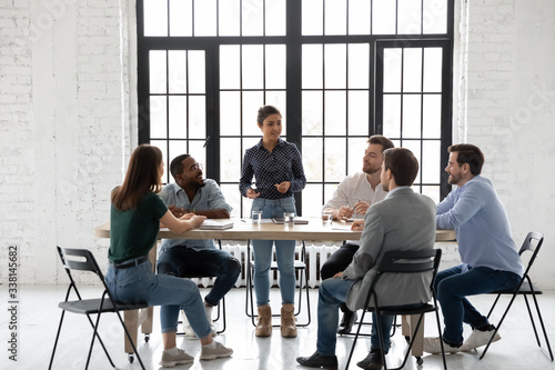 Diverse multiracial businesspeople sit at desk in office brainstorm discuss business ideas together, multiethnic colleagues gather at briefing talk negotiate at team meeting, teamwork concept
