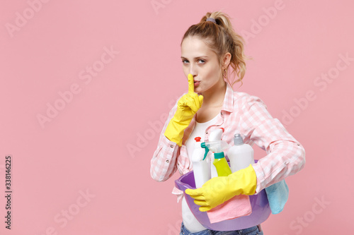Secret girl housewife in rubber gloves hold basin with detergent bottles washing cleansers doing housework isolated on pink background. Housekeeping concept Say hush quiet finger on lips shhh gesture.