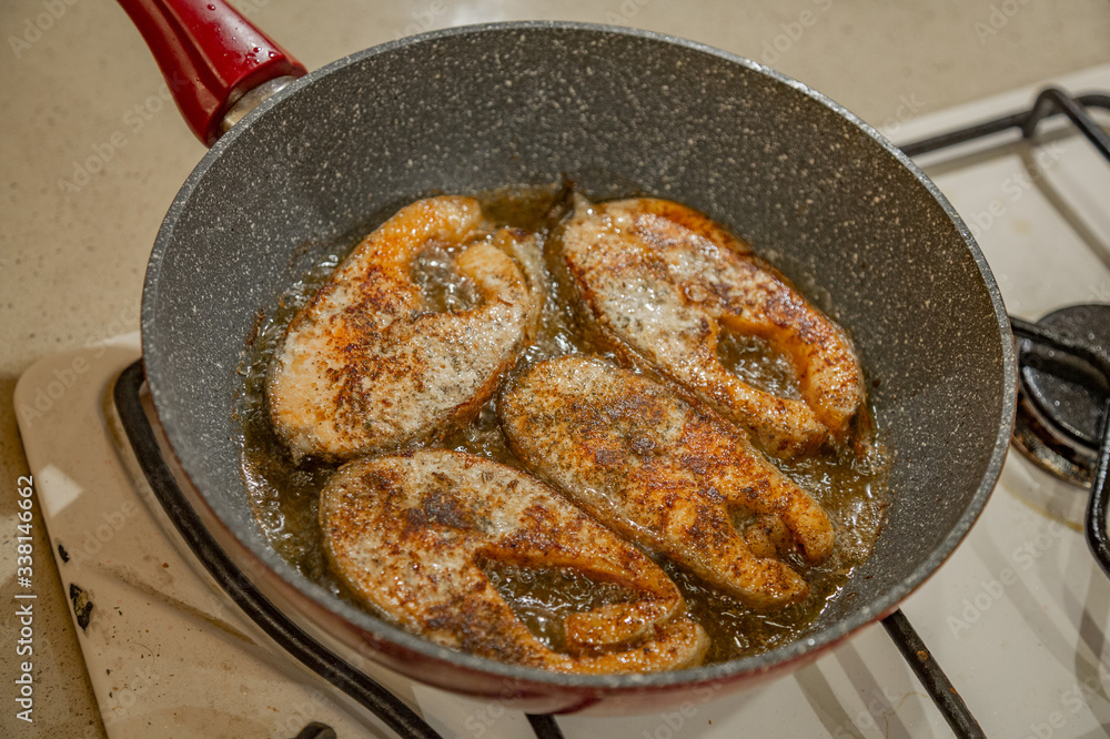 A steak of delicious fish varieties is fried in a frying pan on a kitchen gas stove