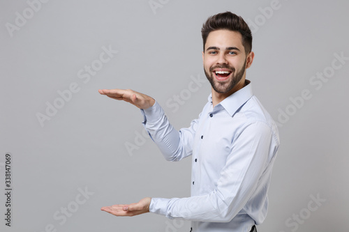 Cheerful young unshaven business man in light shirt isolated on grey background. Achievement career wealth business concept. Mock up copy space. Gesturing demonstrating size with vertical workspace.