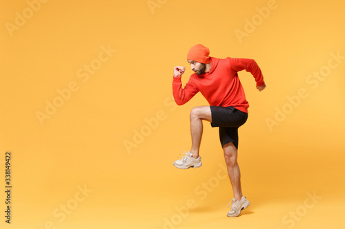 Side view of young bearded fitness sporty guy sportsman in hat, hoodie, shorts spend weekend in home gym isolated on yellow background in studio. Workout sport motivation lifestyle concept. Running.