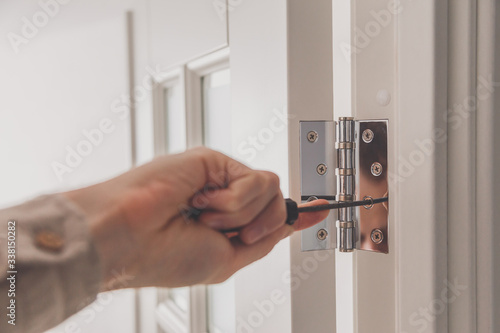 Obraz na płótnie Man remove the door. Twists self-tapping screw with a screwdriver. Stainless door hinges on a white door w salonie
