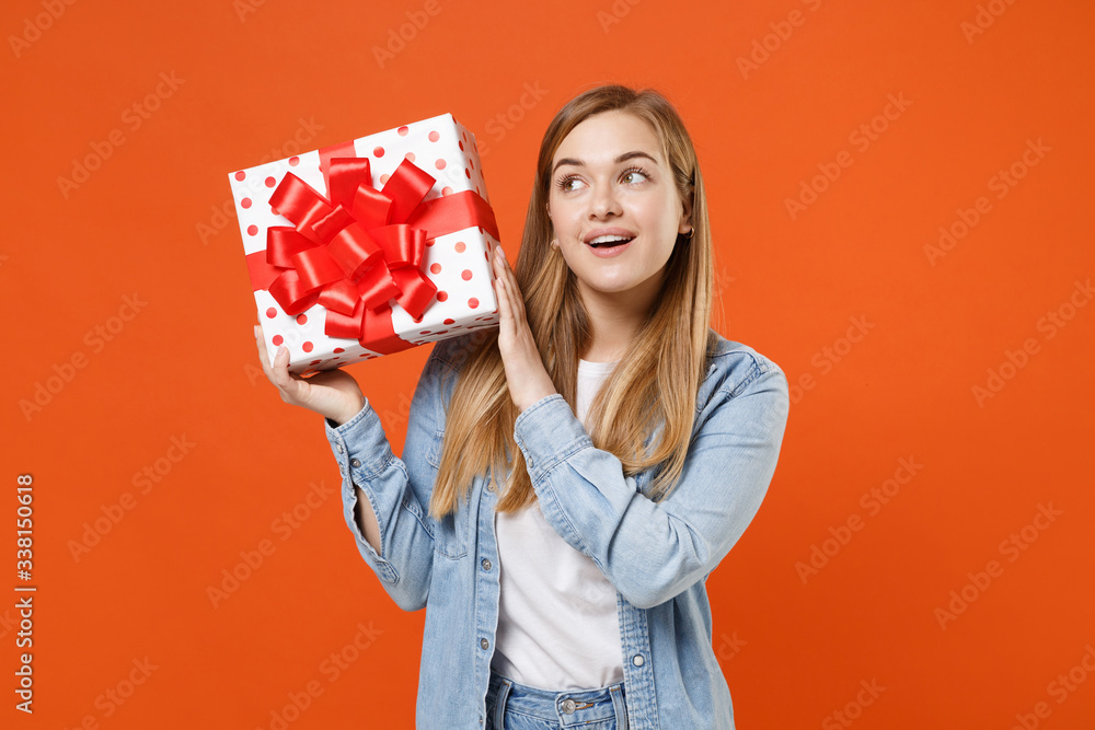 Pensive young woman girl in casual denim clothes isolated on orange wall background. Valentine's Day Women's Day birthday holiday concept. Hold red present box with gift ribbon bow, looking up aside. Pensive young woman girl in casual denim clothes isolated on orange wall background. Valentine's Day Women's Day birthday holiday concept. Hold red present box with gift ribbon bow, looking up aside.