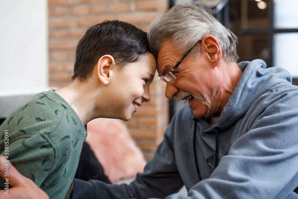 Fototapeta premium Happy grandfather sit on sofa and enjoy spending time with preschooler grandson at home, looking eyes to eyes