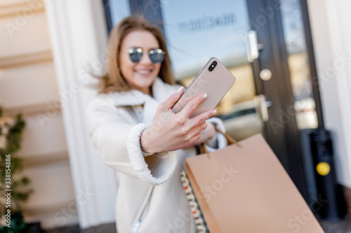 Selfie time, close up photo, young fashionable woman with shopping package walking in the city and make a shoot