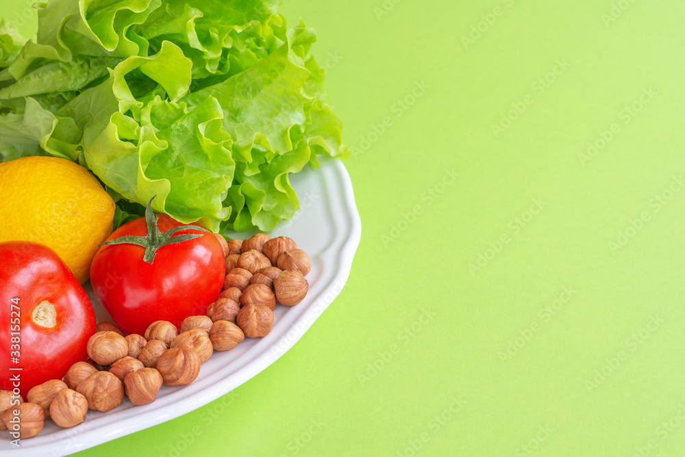 Keto diet. Juicy tomatoes, lemon, lettuce and nuts are on a white platter, on a green background.Horizontal, copy space Keto diet. Juicy tomatoes, lemon, lettuce and nuts are on a white platter, on a green background.Horizontal, copy space