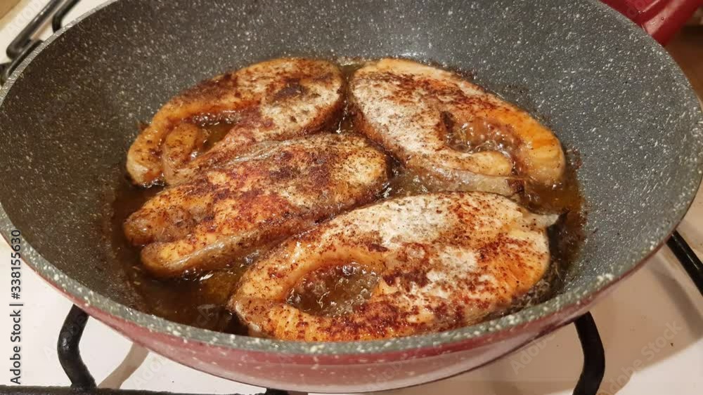 A steak of delicious fish varieties is fried in a frying pan on a kitchen gas stove A steak of delicious fish varieties is fried in a frying pan on a kitchen gas stove