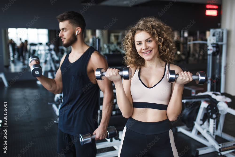 Beautiful young sporty couple trainer and woman showing muscle and workout in gym during training Beautiful young sporty couple trainer and woman showing muscle and workout in gym during training