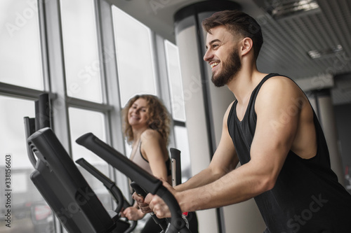 Handsome fitness instructor is running with his attractive client how to work out on an exercise bike in gym