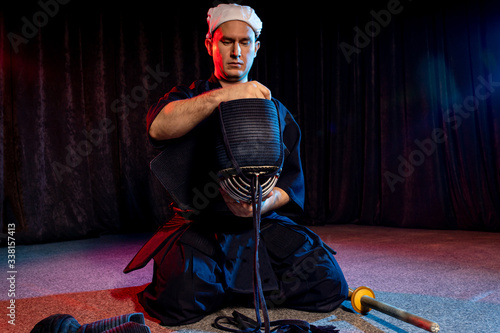 caucasian kendo fighter sit on the floor before fighting, wearing special kendo dress and using all equipment, bamboo sword shinai. japanese martial art as hobby photo