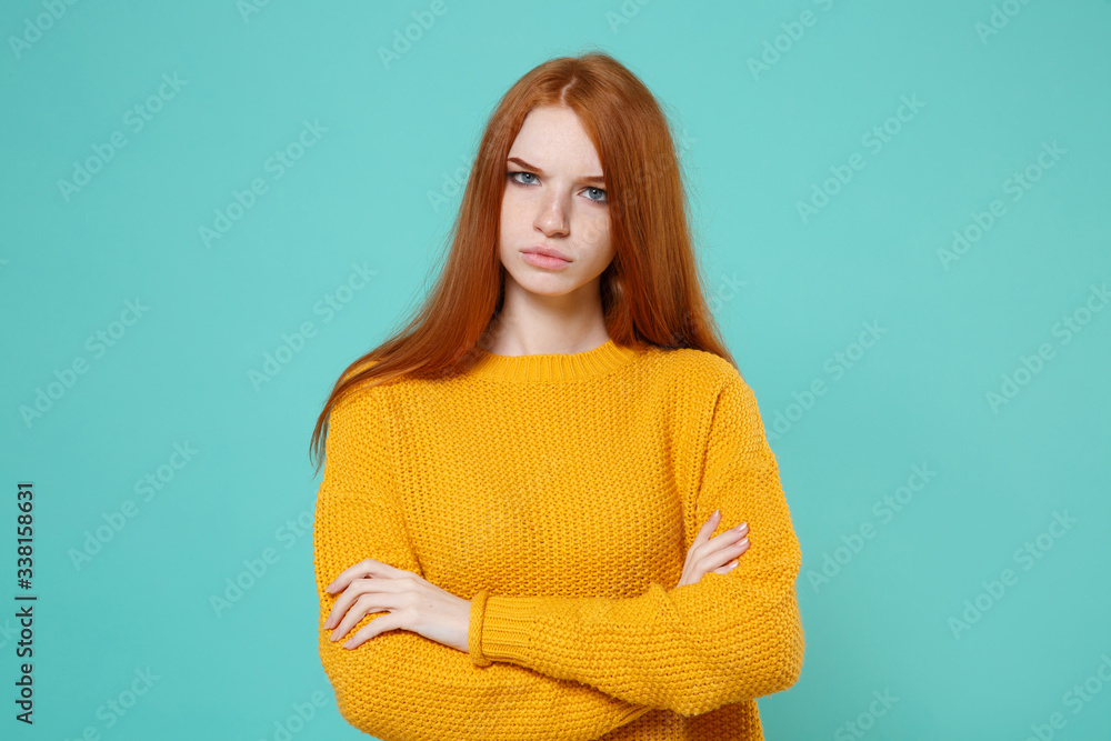 Displeased young redhead woman girl in yellow sweater posing isolated on blue turquoise wall background studio portrait. People emotions lifestyle concept. Mock up copy space. Holding hands crossed. Displeased young redhead woman girl in yellow sweater posing isolated on blue turquoise wall background studio portrait. People emotions lifestyle concept. Mock up copy space. Holding hands crossed.
