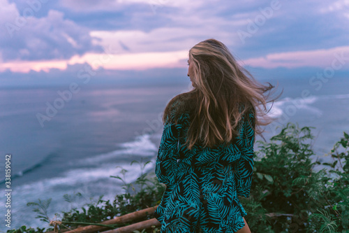 A beautiful girl stands on a cliff overlooking the waves of the blue ocean. Tropical paradise and exotic nature on the island of Bali. Model with different emotions of happiness and joy. photo