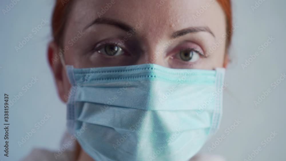 Close-up of a nurse's face in a protective mask. Young female doctor looking at the camera. Steadicam shot. Zoom out. Close-up of a nurse's face in a protective mask. Young female doctor looking at the camera. Steadicam shot. Zoom out.