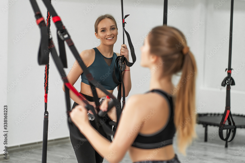 Professional expert ,training total body resistance exercises trainer training pull up together in gym. Group of sportive woman exercising with trx gym equipment with trainer near by