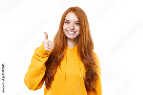 Smiling young redhead woman girl in casual yellow hoodie posing isolated on white wall background studio portrait. People sincere emotions lifestyle concept. Mock up copy space. Showing thumb up.