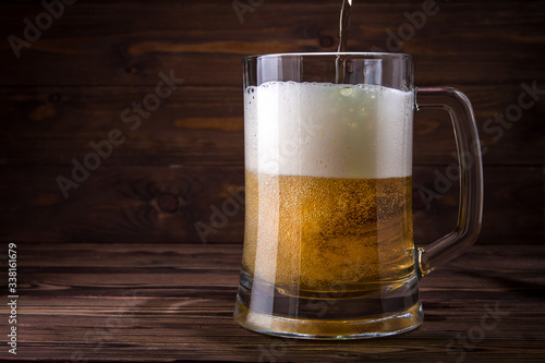 Light beer is poured into a mug on a wooden table. Beer in a mug.