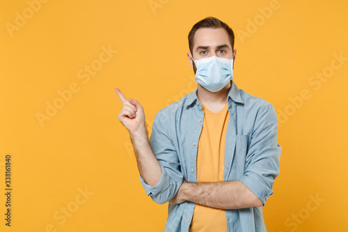 Young man in sterile face mask posing isolated on yellow background studio portrait. Epidemic pandemic spreading coronavirus 2019-ncov sars covid-19 flu virus concept. Pointing index finger aside up.