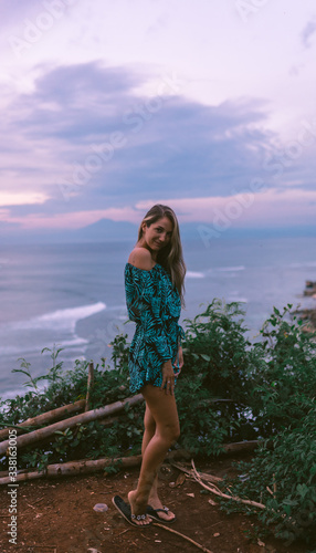 A beautiful girl stands on a cliff overlooking the waves of the blue ocean. Tropical paradise and exotic nature on the island of Bali. Model with different emotions of happiness and joy. photo