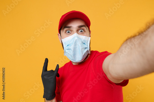 Close up delivery man in red cap blank t-shirt uniform sterile face mask gloves isolated on yellow background studio Guy employee doing selfie shot Service pandemic coronavirus virus 2019-ncov concept